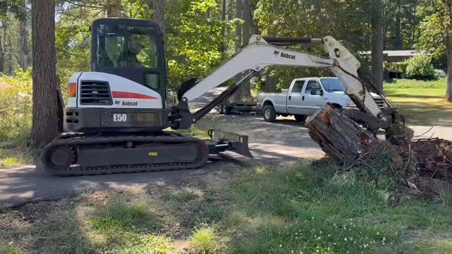 Bobcat E50 mini excavator lifting a large wind-damaged stump on a residential property in Linn County, Oregon